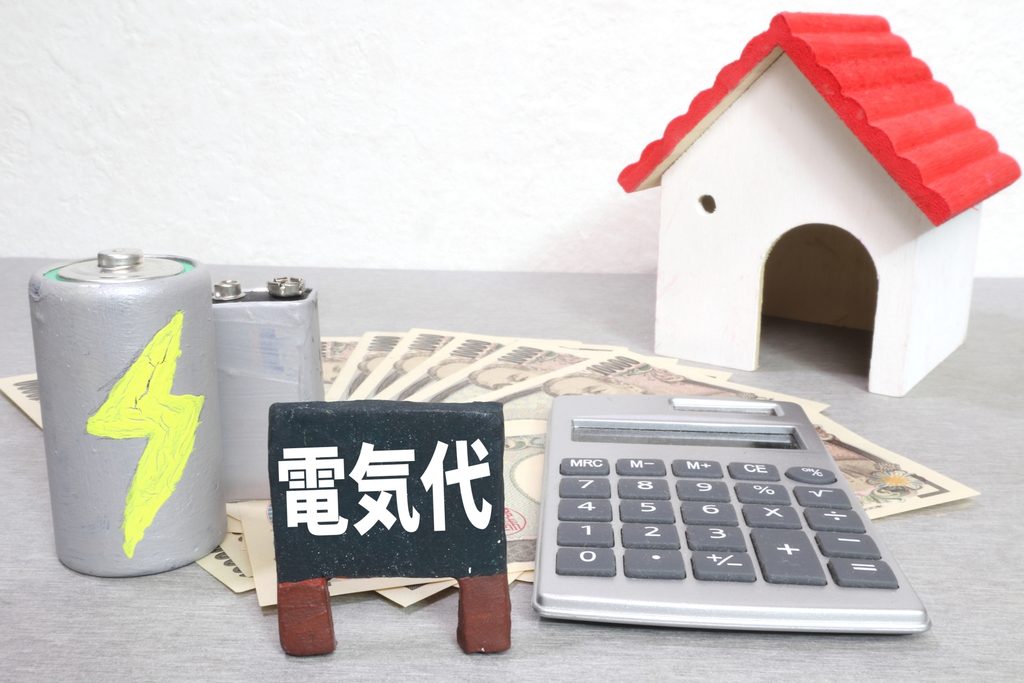 電気代と書かれた看板、電池、電卓、紙幣、家の模型を使って電気料金を表現した画像